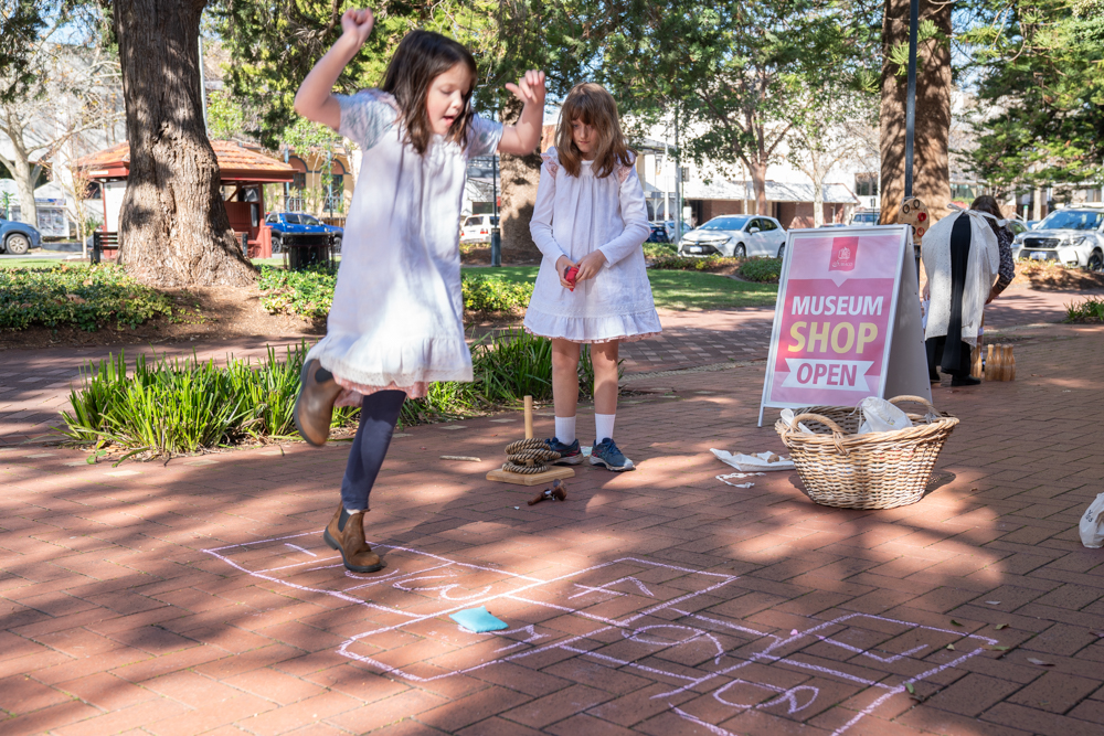 Two young girls playing hop scotch dressed in old fashioned smocks
