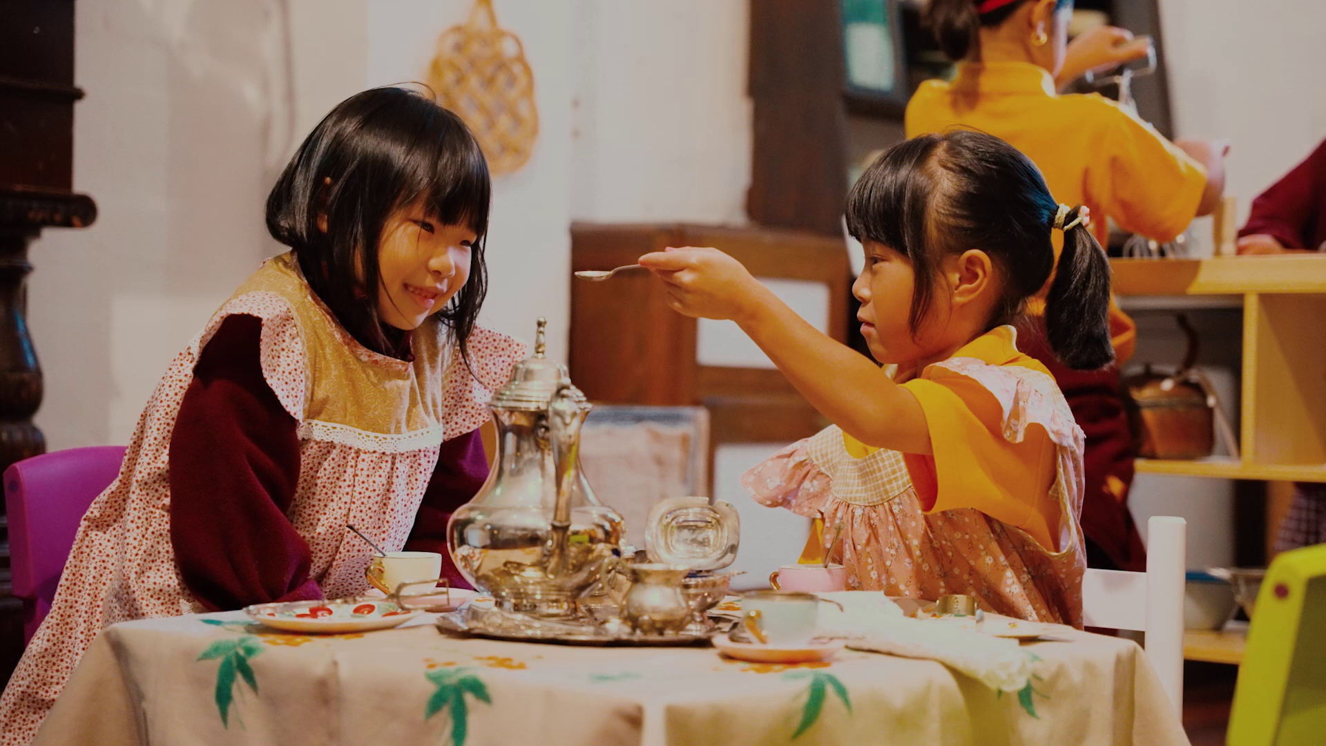 Two young girls playing with a silver tea set in old fashioned smocks